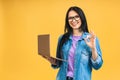 Portrait of happy young beautiful surprised woman with glasses standing with laptop isolated on yellow background Royalty Free Stock Photo
