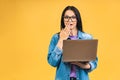 Portrait of happy young beautiful surprised woman with glasses standing with laptop isolated on yellow background. Royalty Free Stock Photo