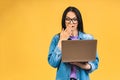 Portrait of happy young beautiful surprised woman with glasses standing with laptop isolated on yellow background Royalty Free Stock Photo