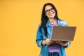 Portrait of happy young beautiful surprised woman with glasses standing with laptop isolated on yellow background Royalty Free Stock Photo