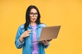 Portrait of happy young beautiful surprised woman with glasses standing with laptop isolated on yellow background Royalty Free Stock Photo