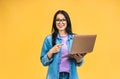 Portrait of happy young beautiful surprised woman with glasses standing with laptop isolated on yellow background. Royalty Free Stock Photo