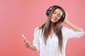 Portrait of a happy young beautiful woman posing  over pink wall background listening music with wireless earphones using Royalty Free Stock Photo