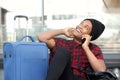 Happy young black man sitting on floor at station with travel bags and talking with mobile phone Royalty Free Stock Photo