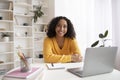 Portrait of happy young black woman sitting at desk with study materials and laptop computer, smiling at camera indoors Royalty Free Stock Photo