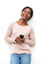 Happy young black woman standing against white wall with cellphone in hand Royalty Free Stock Photo