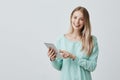 Portrait of happy young blonde business woman in casual clothes using tablet isolated against gray background. Smiling Royalty Free Stock Photo