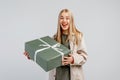 Portrait of Happy young blonde woman in trendy shirt holding big green gift box and looking at the camera over gray background Royalty Free Stock Photo