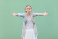 Portrait of happy young blonde woman in white shirt, skirt, and striped blouse with eyeglasses standing with raised arms, smiling Royalty Free Stock Photo