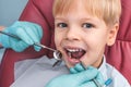 Portrait of happy young boy sitting in dental chair, dentist holding in hands in blue gloves mouth mirror and periodontal explorer