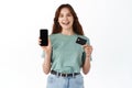 Portrait of a happy young brunette girl showing plastic credit card while holding mobile phone isolated over white Royalty Free Stock Photo