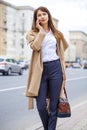 Portrait of happy young brunette woman in beige coat talking on Royalty Free Stock Photo