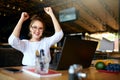 Portrait of happy young business woman celebrating success with arms up in front of laptop. Mixed race female won a lot Royalty Free Stock Photo