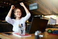 Portrait of happy young business woman celebrating success with arms up in front of laptop. Mixed race female won a lot Royalty Free Stock Photo