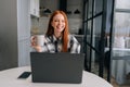Portrait of happy young business woman remote working or studying on laptop computer sitting at table, holding in hand Royalty Free Stock Photo