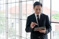 Portrait of happy young businessman looking at business document in tablet, standing near the window in office background Royalty Free Stock Photo