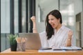 Portrait of a happy young businesswoman celebrating success with arms raised in front of a laptop, fists clenched. The Royalty Free Stock Photo