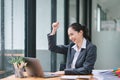 Portrait of a happy young businesswoman celebrating success with arms raised in front of a laptop, fists clenched. The Royalty Free Stock Photo