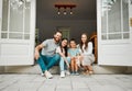 Portrait of a happy young caucasian family of four sitting at their front door smiling and looking at the camera. Two Royalty Free Stock Photo