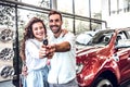 Portrait of a happy young couple hugging in a car salon showing car keys to a newly bought vehicle Royalty Free Stock Photo