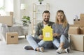 Happy young couple sitting on floor in their new home and holding miniature paper house