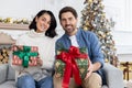 Portrait of a happy young couple sitting on the sofa at home, holding Christmas gift boxes and smiling at the camera Royalty Free Stock Photo