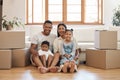 Portrait of happy young family with two kids sitting in new home, stacked cardboard boxes in living room. Mixed race Royalty Free Stock Photo