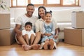 Portrait of happy young family with two kids sitting in new home, stacked cardboard boxes in living room. Mixed race Royalty Free Stock Photo