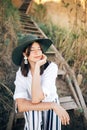 Portrait of happy young fashionable woman relaxing on tropical island. Stylish boho girl in hat sitting on wooden stairs at sandy Royalty Free Stock Photo