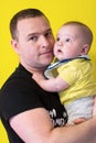 Portrait of happy young father holding baby isolated on yellow Royalty Free Stock Photo