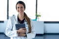 Happy young female doctor smiling and looking at camera while digital tablet and standing in the consultation Royalty Free Stock Photo