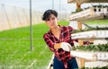 Portrait of happy young female farmer carring cart with trays of sprouts at modern farm