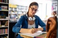 Portrait of happy young female student taking notes from a book at college library. Royalty Free Stock Photo