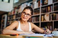 Portrait of happy young female student taking notes from a book at college library. Royalty Free Stock Photo