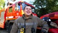 Portrait of happy young fireguard in uniform against background of a fire truck. Male firefighter looking into camera