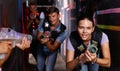 Portrait of happy young friends playing laser tag game with laser guns in dark corridor