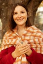 Portrait of happy young gorgeous woman holding scarf with hands, standing near tree in forest park. Vertical. Autumn. Royalty Free Stock Photo