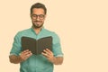 Portrait of happy young handsome bearded Indian businessman reading book Royalty Free Stock Photo