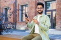 Portrait of a happy young Hindu man using a credit card and phone, sitting outside on a bench and smiling at the camera Royalty Free Stock Photo