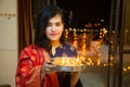 Portrait of Happy Young indian beautiful woman hold plate/thali with diya/clay oil lamps wearing traditional dress,standing indoor Royalty Free Stock Photo