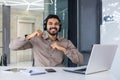 Portrait of a happy young Indian man sitting at a desk in the office, working on a laptop, looking smiling at the camera Royalty Free Stock Photo