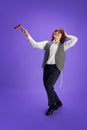 Portrait of happy young Jewish man in formal suit and kippah dancing with grogger against purple studio background. Royalty Free Stock Photo