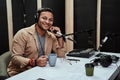 Portrait of happy young male radio host having a drink, smiling at camera while moderating a live show Royalty Free Stock Photo