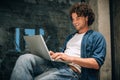 Portrait of happy young man with curly hair using laptop for working online. Smart freelance man chatting online with clients. Royalty Free Stock Photo