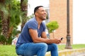 Happy young man with mobile phone sitting on sidewalk and looking away Royalty Free Stock Photo