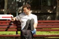 Happy young man sitting on bench outdoors with travel bag and mobile phone Royalty Free Stock Photo