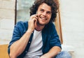 Portrait of happy young man stitting on the bench outdoors and talking on mobile phone. Happy male with curly hair resting outside Royalty Free Stock Photo