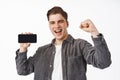 Portrait of happy young man winning on mobile phone, yelling from victory, fist pump and smiling pleased, showing Royalty Free Stock Photo