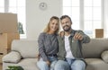 Happy young couple sitting on couch in new apartment and showing key to their new home Royalty Free Stock Photo