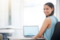 Portrait of a Happy young mixed race businesswoman smiling while enjoying working on a laptop sitting in a chair in an Royalty Free Stock Photo